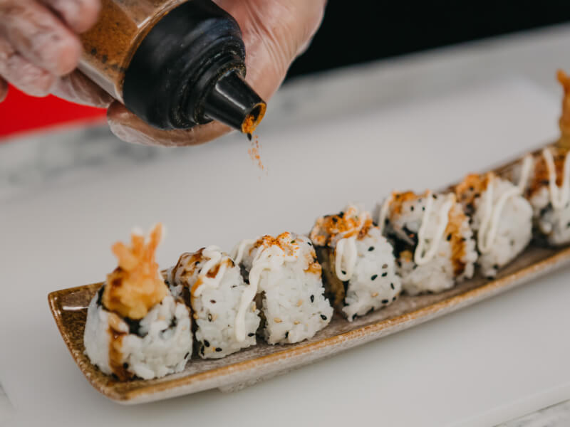 A close up image of sauce being drizzled on sushi. 